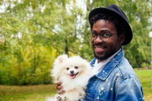 African American man hugging his fluffy spitz in park.